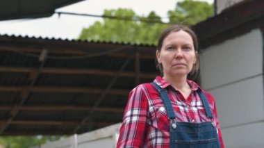 Çiftlikte poz veren ciddi bir kadın çiftçi. Kendine güvenen kadın çiftlik işçisi takılarak gömlek ve kot tulum kamera bakarak, silah geçti