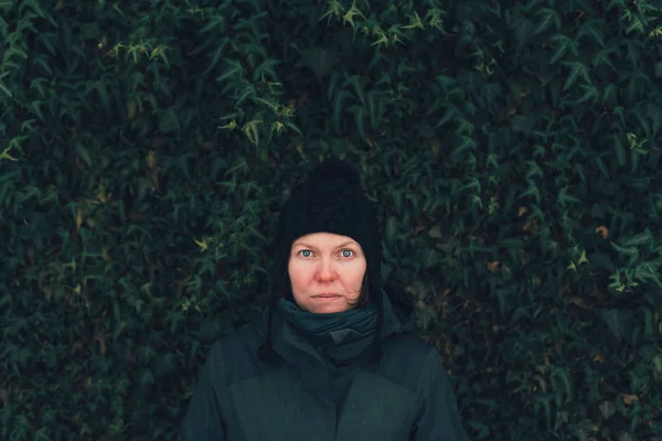 Serious woman in winter clothing against the ivy wall — Stock Photo, Image