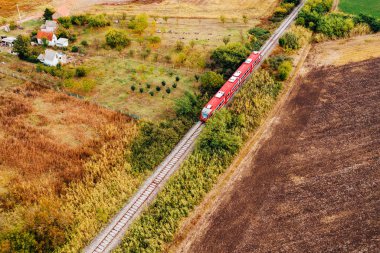 Kırmızı yolcu treni kırsal alanda ilerliyor, hava manzaralı.