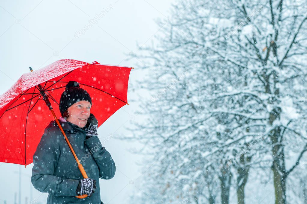 Satisfied woman talking on mobile phone under umbrella in snow