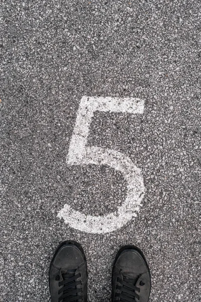 Człowiek stojący nad numerem pięć odcisk na asfaltowej drodze — Zdjęcie stockowe