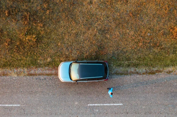 Vrouw en auto op de weg door grasland, vanuit de lucht gezien — Stockfoto