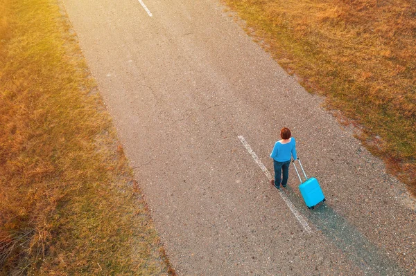 Woman pulling travel suitcase luggage on road in autumn sunset — Stock Photo, Image