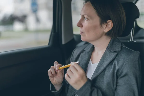 Businesswoman waiting at car back seat and playing with pencil to overcome anxiety