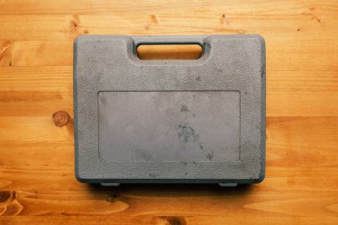 Ahşap çalışma masasının üstündeki eski kirli plastik alet çantası, üst manzara.