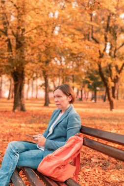 Güz parkı bankında cep telefonuna mesaj yazan kadın, seçici odaklı sıcak sonbahar renkleri renkli resim