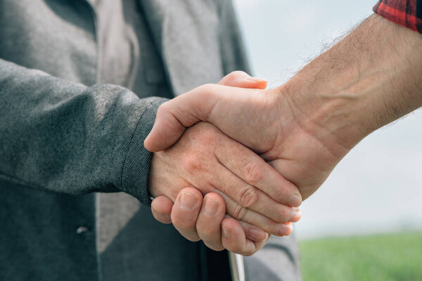Mortgage loan officer and farmer shaking hands upon reaching an agreement for financial allowance application, banker and farm worker in corn maize crop field.