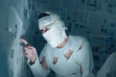 Victim of tabloid journalism and fake news infodemic, conceptual image of man wrapped in bandages surrounded by walls covered with daily newspaper pages clipart