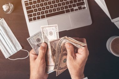 İş adamı, büro masasında Amerikan dolarlarını sayıyor. Paralı erkeklerin üst görüntüsü.