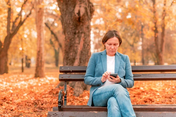 Kobieta Wpisująca Sms Telefon Komórkowy Jesiennej Ławce Parku Ciepłe Kolory — Zdjęcie stockowe