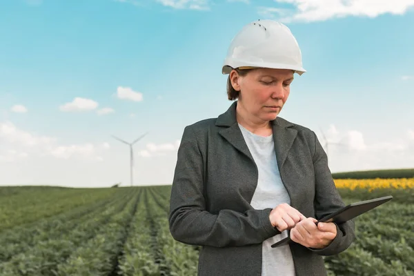 Female engineer with tablet computer on modern wind turbine farm during maintenance project planning