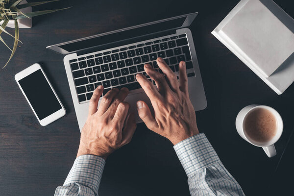 Businessman typing laptop computer keyboard, top view of office desk in morning