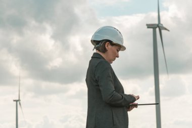 Female engineer with tablet computer on modern wind turbine farm during maintenance project planning clipart