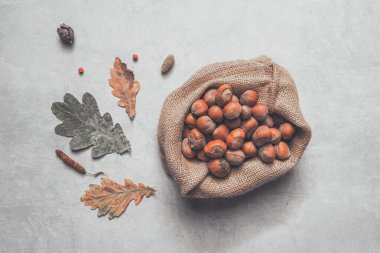 Kuru sonbahar yaprakları ve dallarla süslenmiş kırsal ahşap masa üzerinde çevre dostu çuval içinde kabuklu fındık manzarası