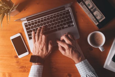 İşadamı dizüstü bilgisayar klavyesini daktilo ediyor, sabahları ofis masasının üstünden çekim yapıyor.