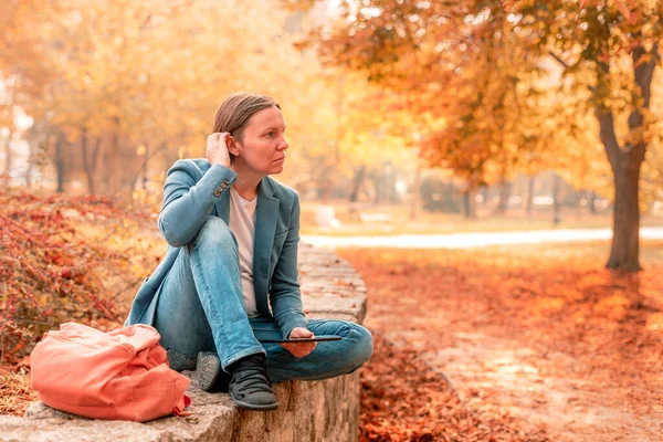 Woman using digital tablet on park bench in autumn during working hours break, selective focus