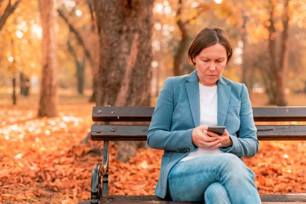 Vrouw Typt Tekst Mobiele Telefoon Herfstparkbank Kopieerruimte Met Selectieve Focus — Stockfoto