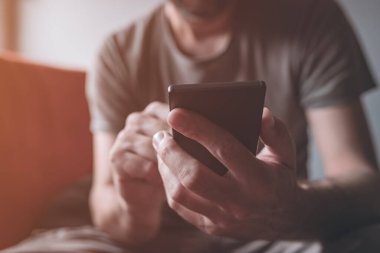 Evde cep telefonu kullanan, akıllı telefon bağımlısı, seçici odaklı erkek ellerini kapatan bir adam.