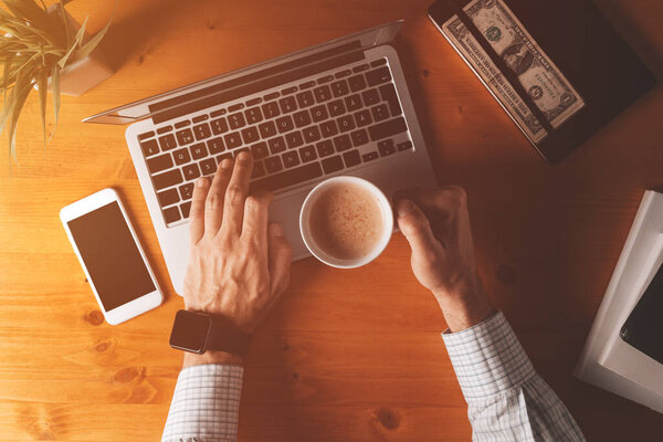 Бизнесмен пьет кофе и печатает клавиатуру ноутбука, снимки офисного стола утром