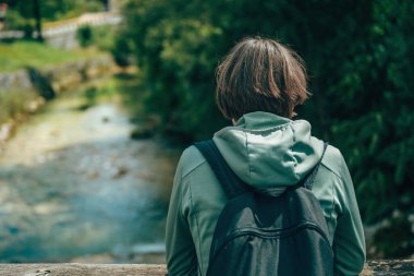 Sırt çantalı kadın yürüyüşçü, Slovenya 'daki dağ nehrine ve geleneksel dağ köyüne hayran. Seçici odak.
