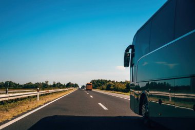 Açık gökyüzünün altındaki otoyolda bir otobüs özgürlüğü, yönü ve sonsuz yolculukları simgeliyor. Güneşli bir günde otoyolda ağaçlar ve trafik olan bir otobüsün yan görüntüsü. Seçici odak.