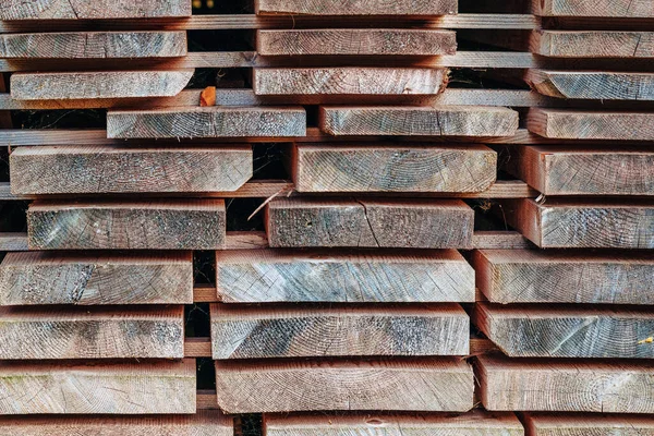 Marangozluk ve ahşap işçiliği için doğal dokuyu ve inşaat malzemelerini göstermek için açık havada dizilmiş tahta yığınları..