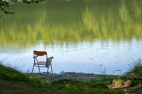 Gone fishing, perhaps, chair left by lake edge. Summer. Background, nobody there in lakeside seat. — Stock Photo, Image