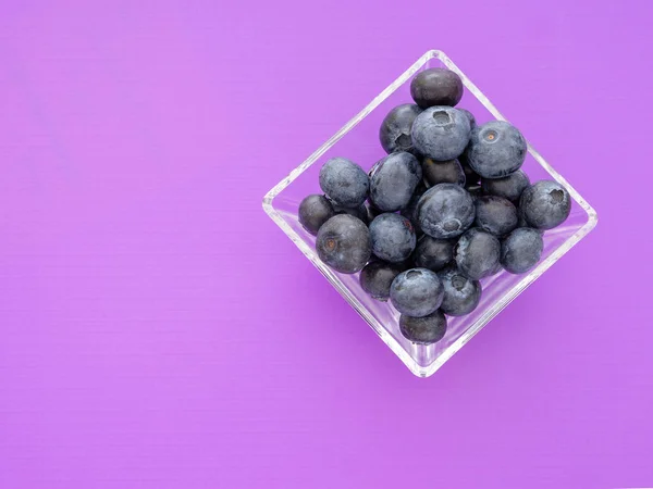 Friska superfood blåbär i fyrkantig glasskål på vackra lila bakgrund. Med copyspace. — Stockfoto