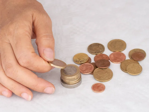 Maduro, mulher mão colocando moedas em uma pilha, heap, em fundo de toalha de mesa branco. Perto. Moedas europeias em euros, contagem de cêntimos, pequena alteração . — Fotografia de Stock