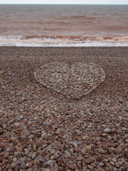在海滩上用鹅卵石制作的大爱心形。垂直裁剪. — 图库照片