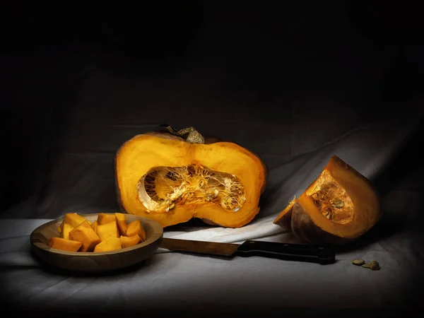 Zucca invernale di mais, zucca, preparata per la cottura, cubetti con semi, coltello. Chiaroscuro, pittura leggera in stile barocco . — Foto Stock