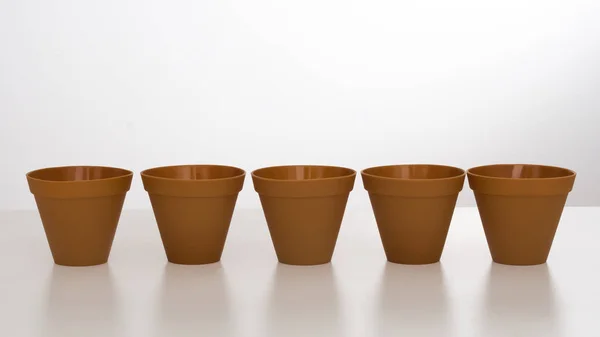 Fila de vasos de flores de plástico no fundo branco com reflexão . — Fotografia de Stock