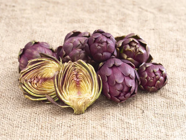 Raw artichokes, Mediterranean vegetable, uncooked on rustic hessian. One cut open to see inside. — 图库照片