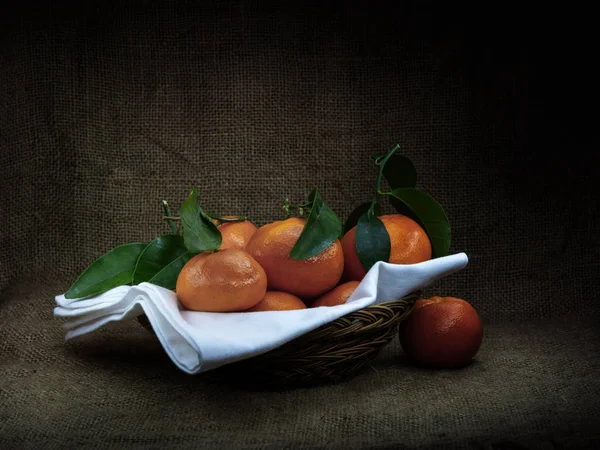 Oranges with leaves in basket, dark ciaroscuro style still life. Fruit on hessian . — Stock Photo, Image