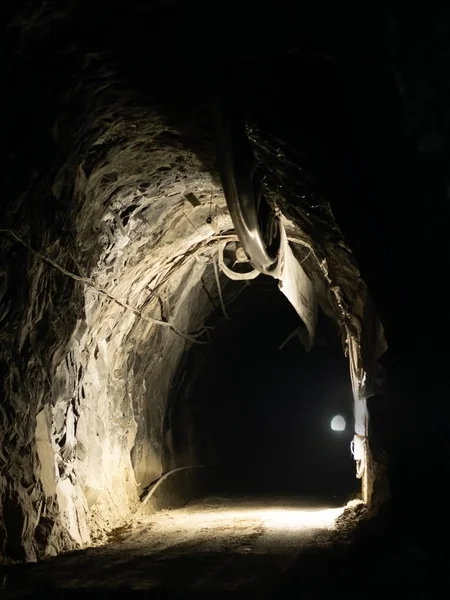 Túnel industrial que conduce de la oscuridad a la luz. Viejo, desbastado, con ventilador . — Foto de Stock