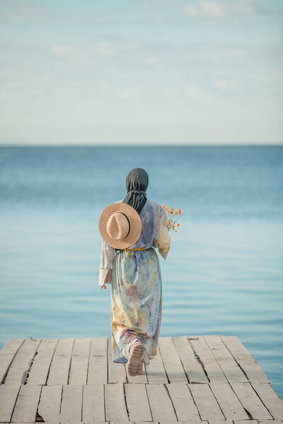 Modest girl in a hat near the seashore on the beach, against the blue sky