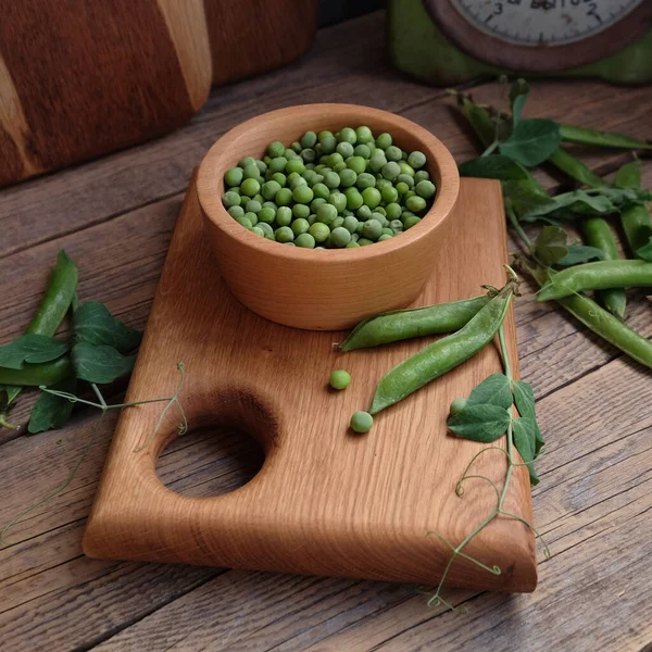 木の鉢の中の緑のエンドウ豆はまな板の上に立つ ストック画像