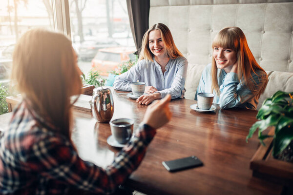 three happy female friends drinking coffee in cafe
