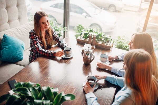 three happy female friends drinking coffee in cafe