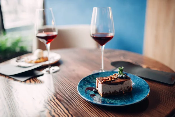 Dessert on a plate and red wine in glass on wooden table. Chocolate cake and alcohol, arrangement of romantic dinner in cafe