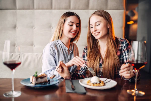 两个微笑的年轻女人在咖啡馆里吃甜饼喝红酒 — 图库照片