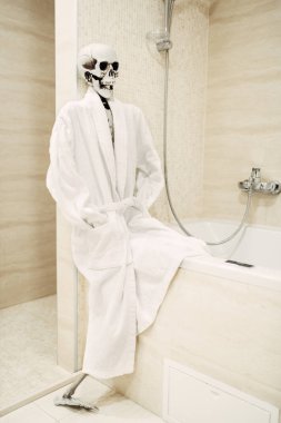 beyaz bornoz banyo banyo kenarında oturan insan iskeleti