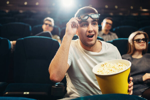 Surprised man with popcorn watching film in cinema. Movie entertainment