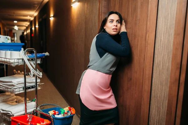 制服のクリーニング女性は好奇心の扉 洗剤が付いているカート ホテル廊下インテリアの背景に耳します 専門清掃 掃除婦の仕事 — ストック写真