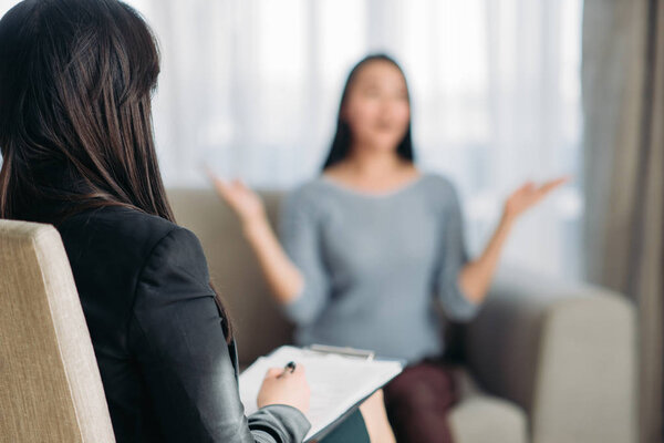 female patient sitting on sofa at psychotherapist. Female doctor writing notes, professional psychology support