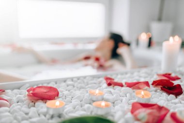 Genç kadın, banyo köpüğü ile yalan gül yaprakları ve yanan mumlar dekor