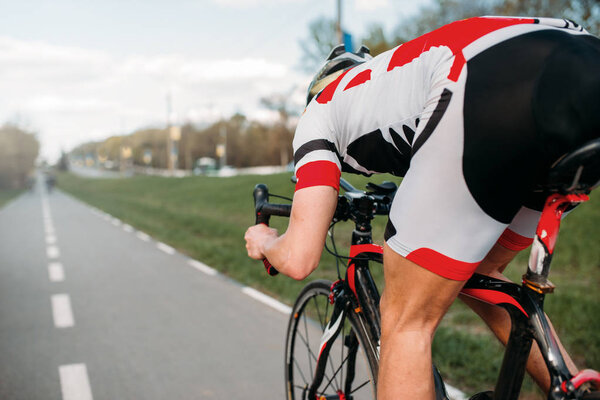 велосипедист в шлеме и спортивной одежде на велосипеде, вид сзади
 