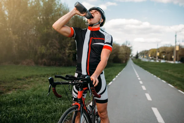男骑自行车在头盔和运动装饮料 而培训 在自行车道上锻炼 在沥青路面上骑车 — 图库照片