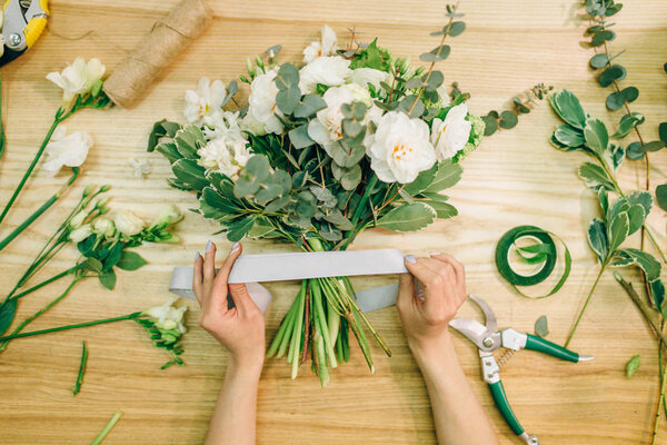 руки флористки, делающей цветочную композицию с обрезкой
