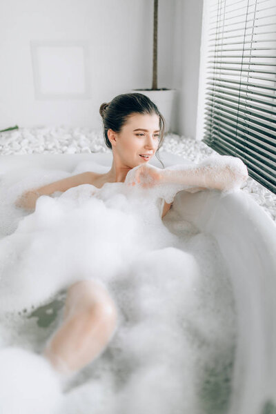 Sexy woman lying in bath with foam, relaxation in luxury bathroom with stone decor